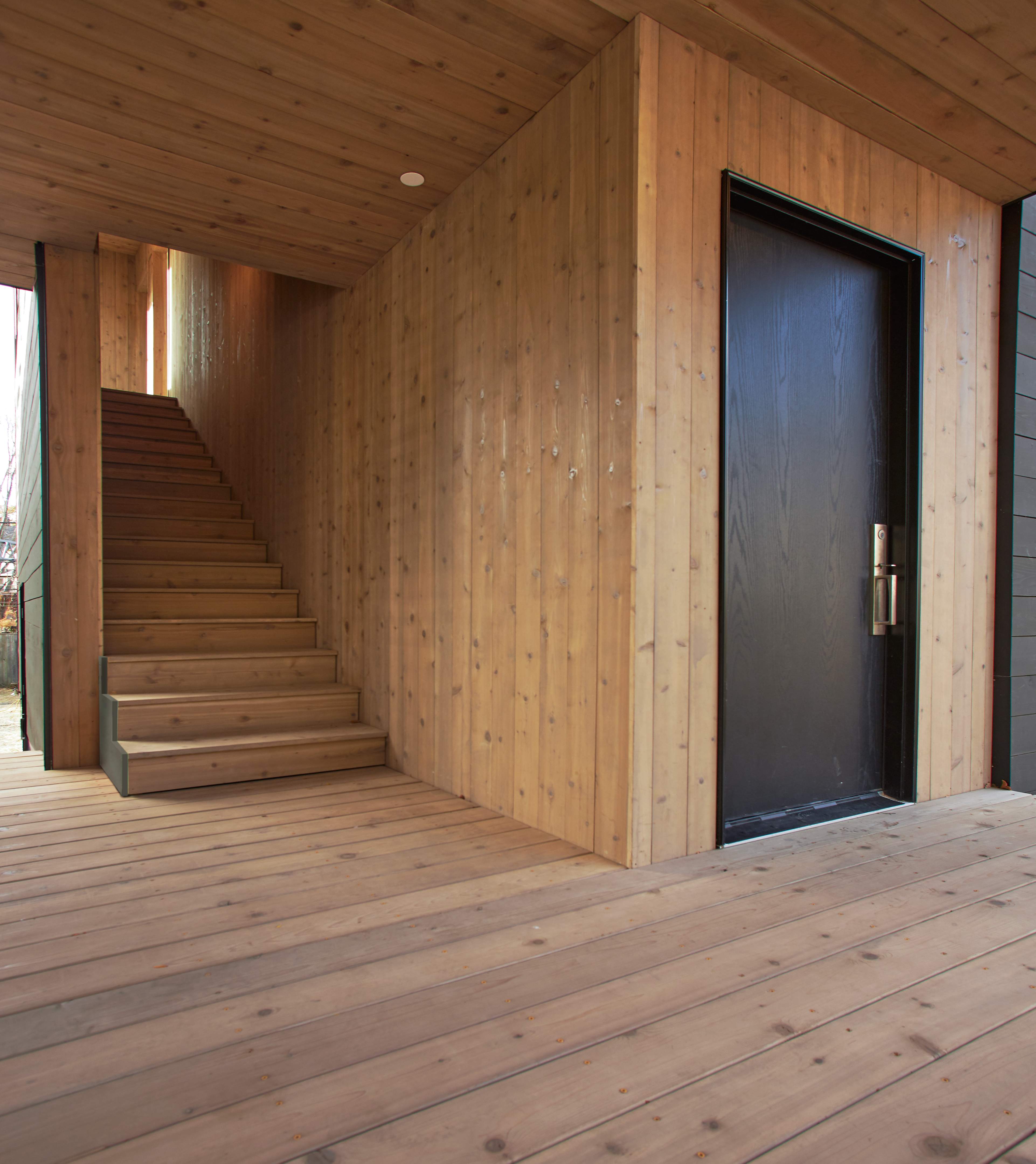 Cedar-clad entryway with wooden staircase and dark front door